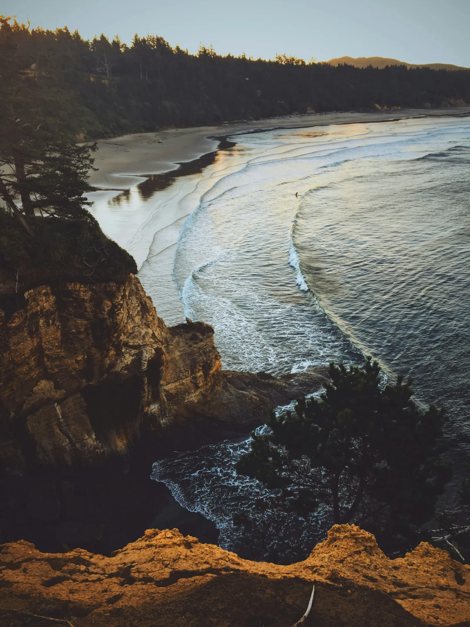 Golden hour over the beach at Otter Rock, a lone surfer paddling out below the cliffs